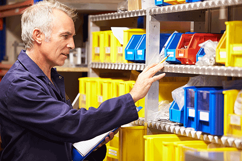 Homme en bleu de travail vérifiant des stocks sur des étagères avec des bacs colorés – gestion de stock en entreprise