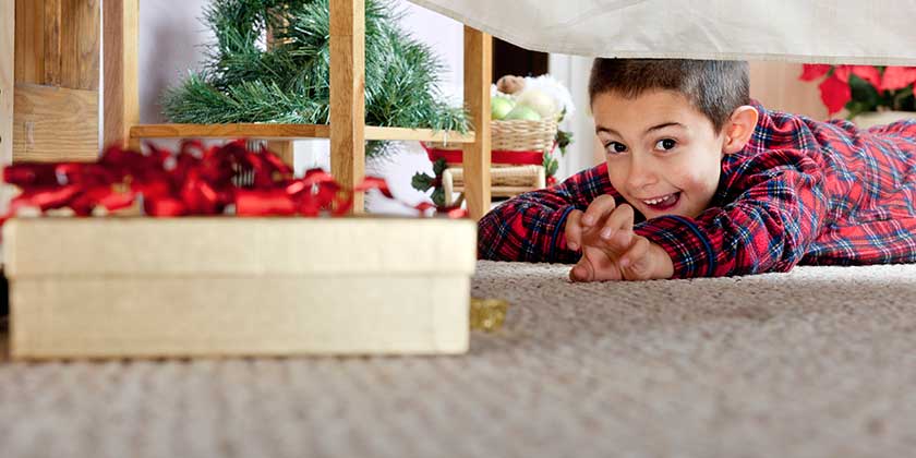 Enfant cherchant des cadeaux de Noël sous un lit – solution de stockage pour préserver la surprise