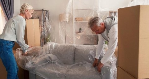 Couple protégeant un canapé avec du plastique avant de le stocker – préparation des meubles pour garde-meuble